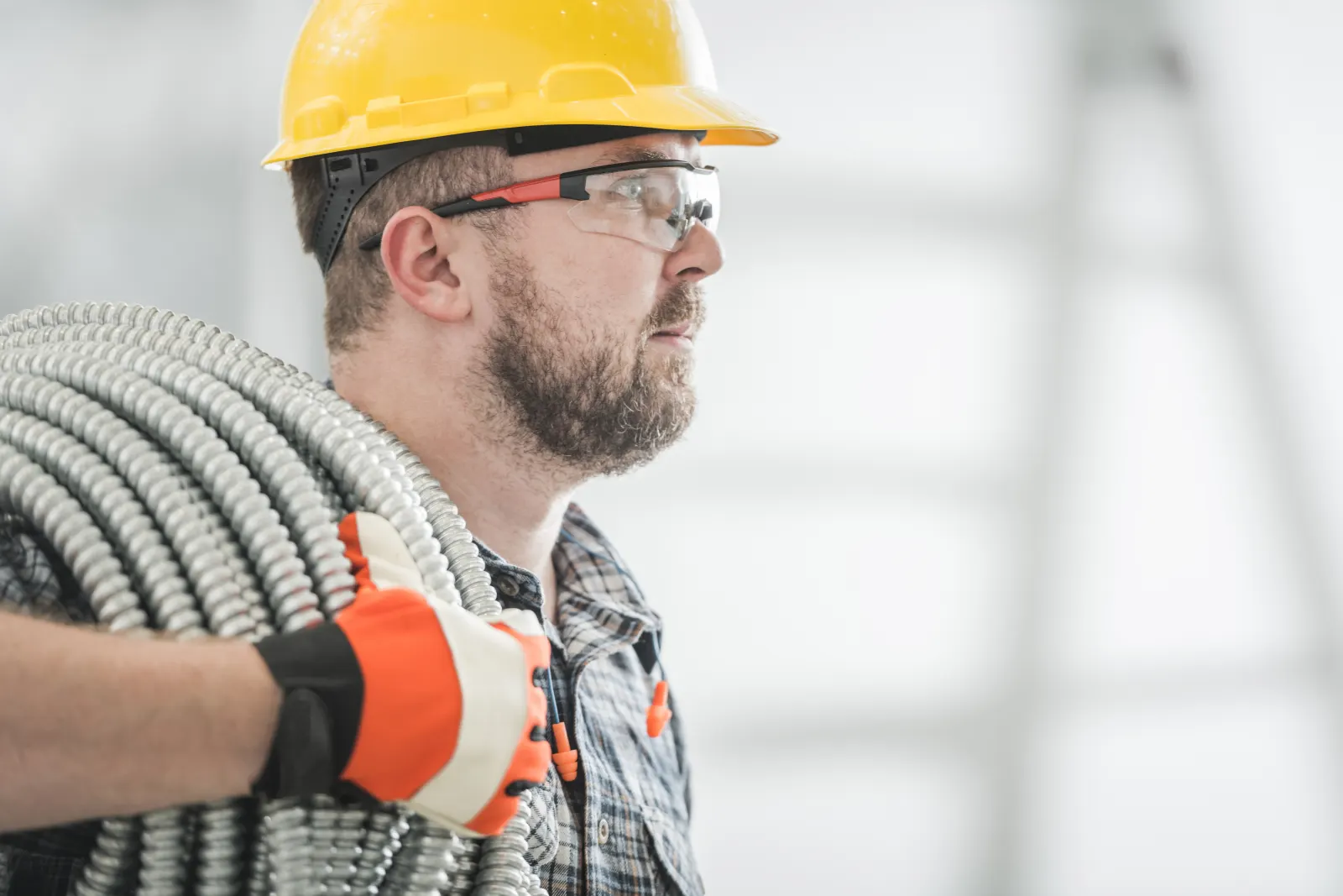 Electrician carrying coiled metal conduit on job site